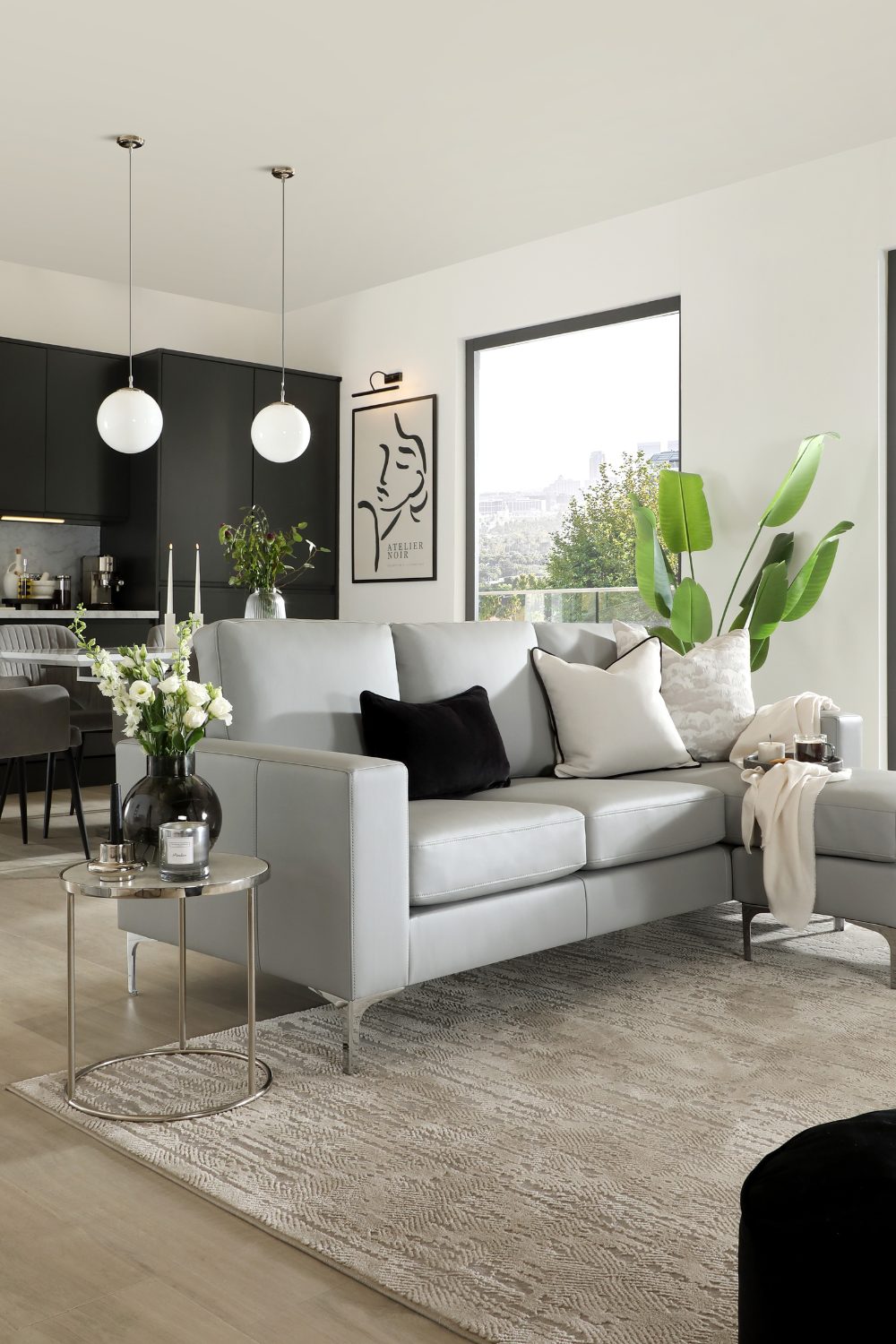 Grey sofa on beige rug in front of window with garden view and black kitchen