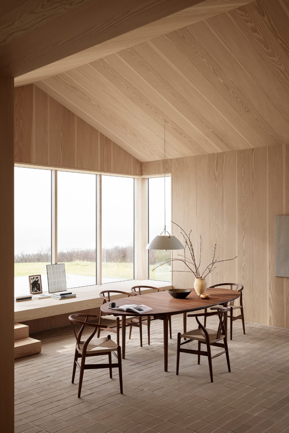 Wooden barn room interior with wooden table and chair, white hanging lamp, and windows with a garden view