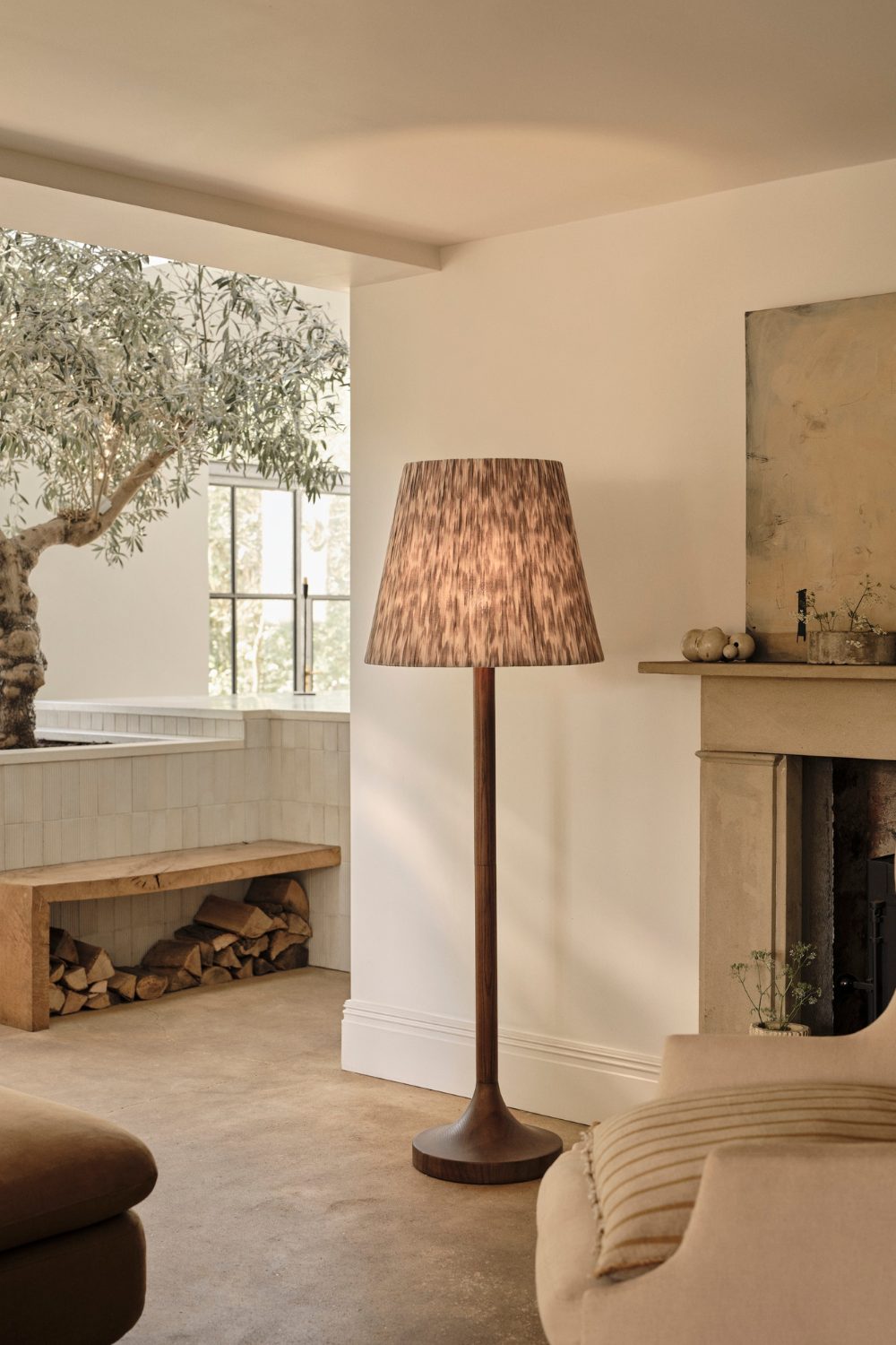 White living room with wooden bench, brown lamp, stone fireplace and small tree
