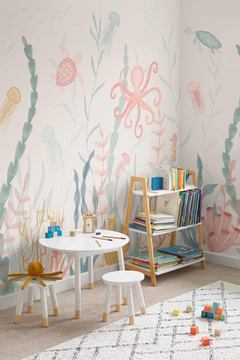Nursery with sealife mural on wall, white table and stools, white rug, and wooden bookshelf
