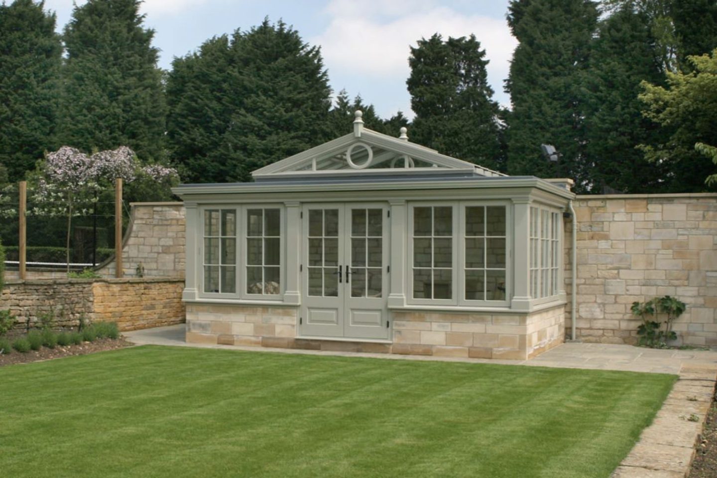 Muted green orangery behind neat lawn and stone wall