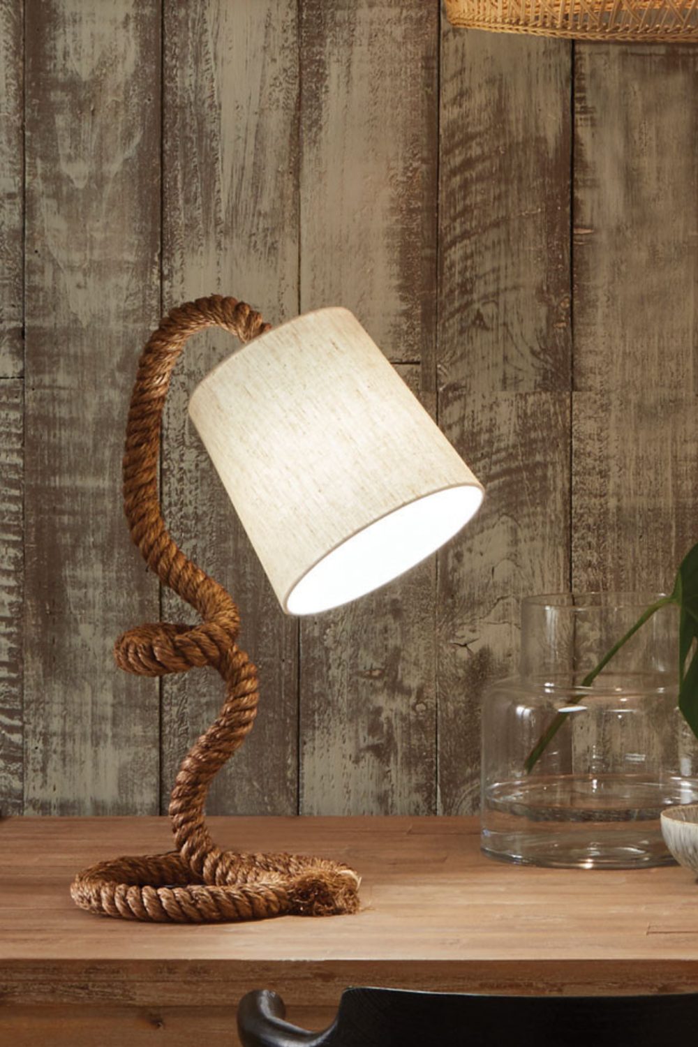 Rope lamp on wooden table next to driftwood wall