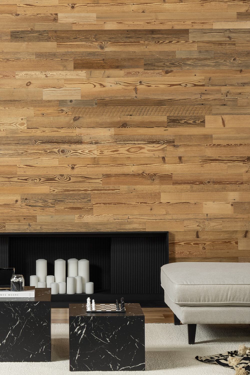 Wooden plank wall behind black marble tables, black fireplace and grey sofa