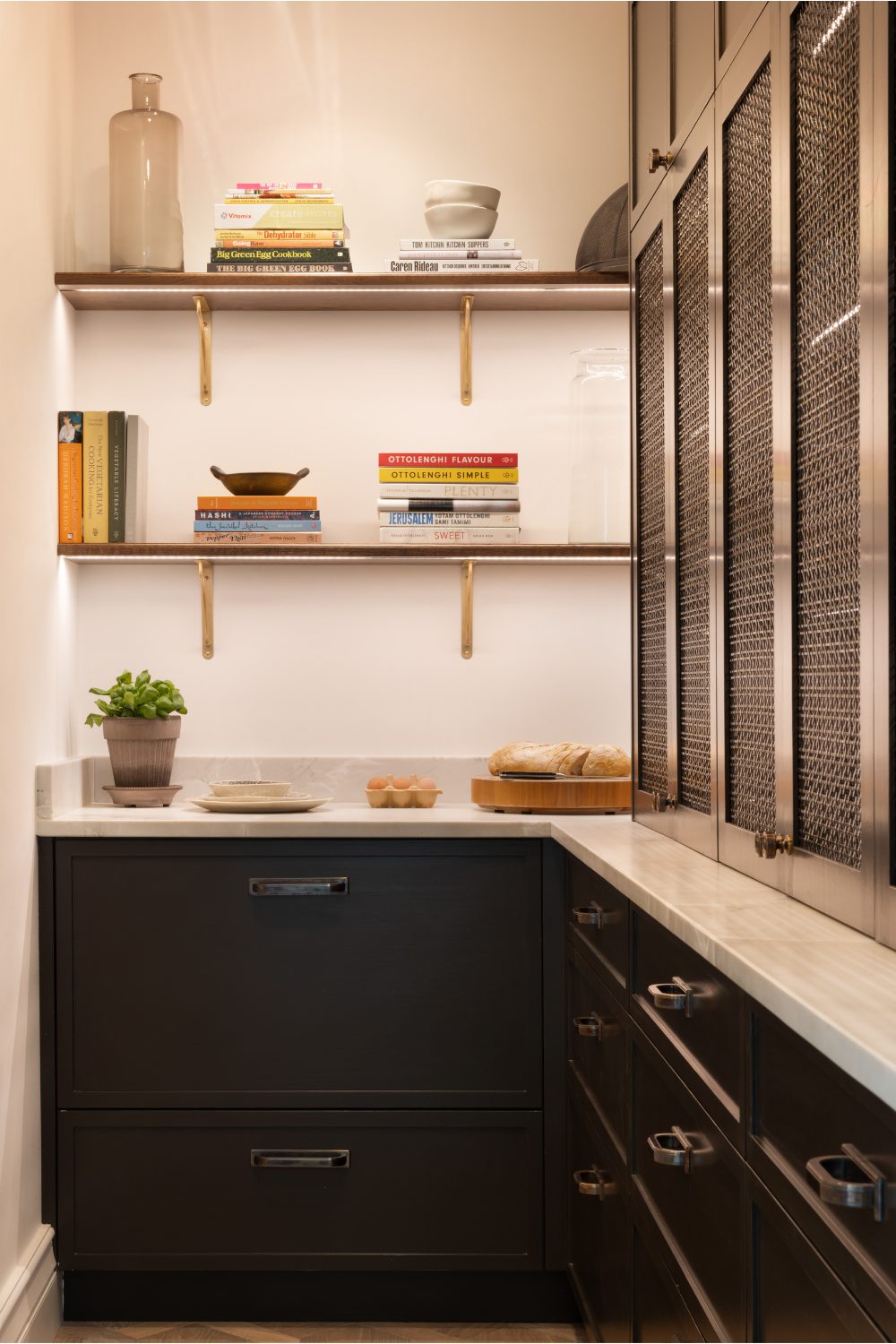 Built-in shelves in white kitchen holding recipe books and bowls above black cabinets