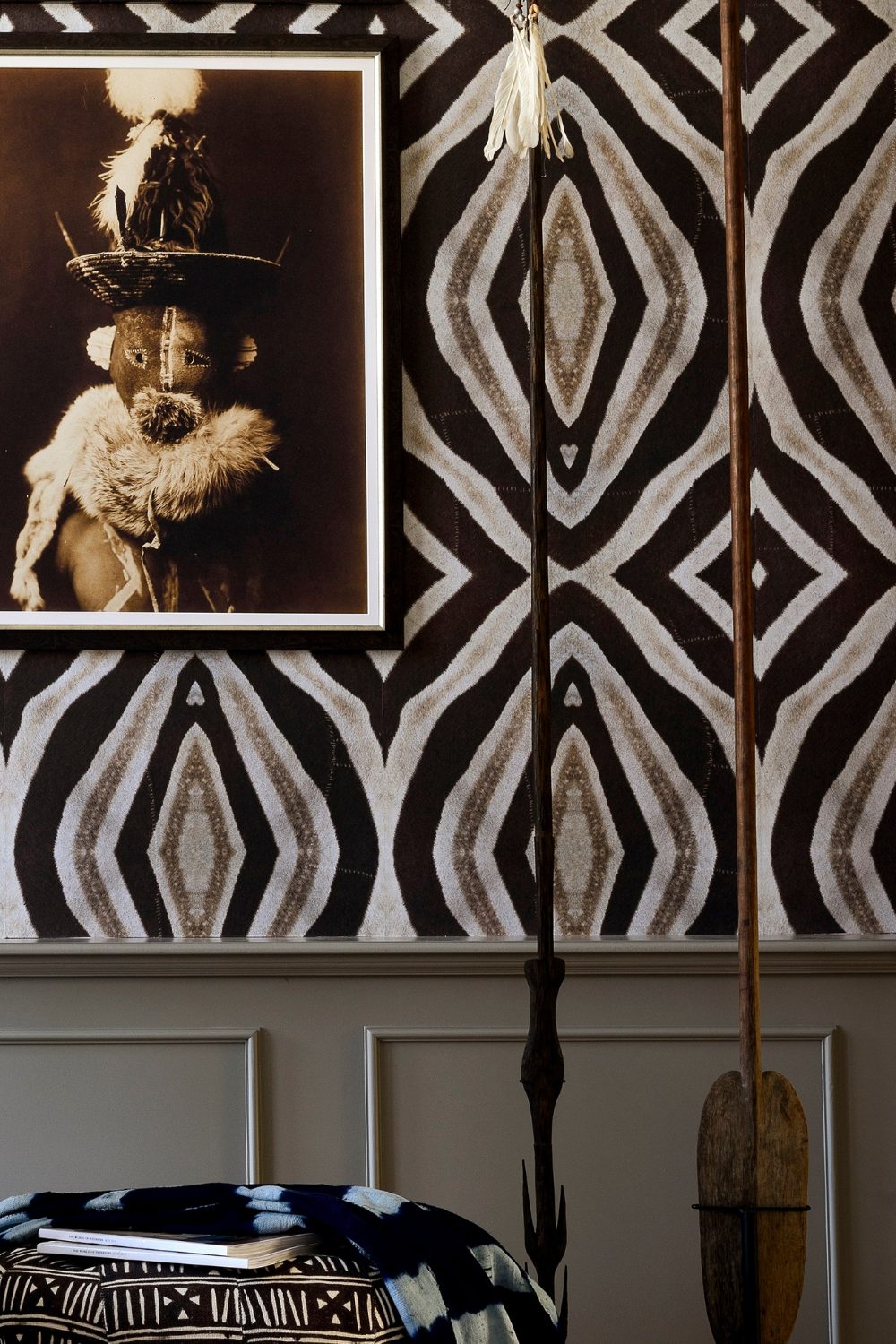 Bold black and white Zulu print wallpaper with a framed photo of masked Zulu tribesman above a black and white print pouffe