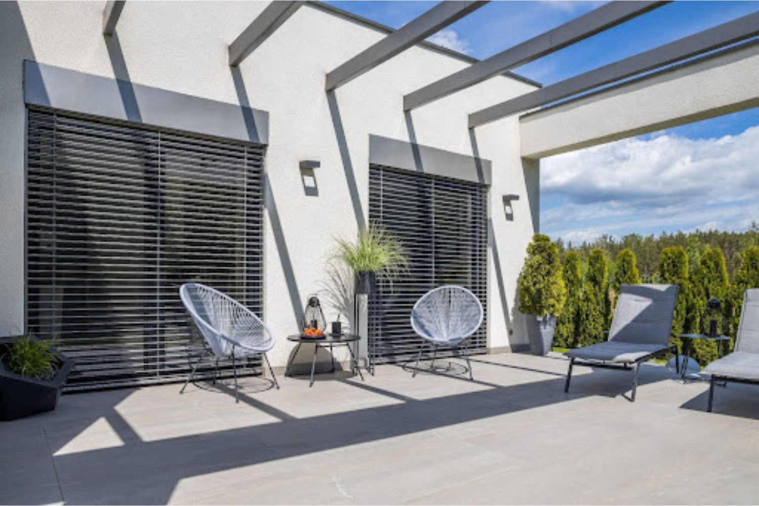 Glass veranda with grey garden chairs, potted trees and views of blue sky