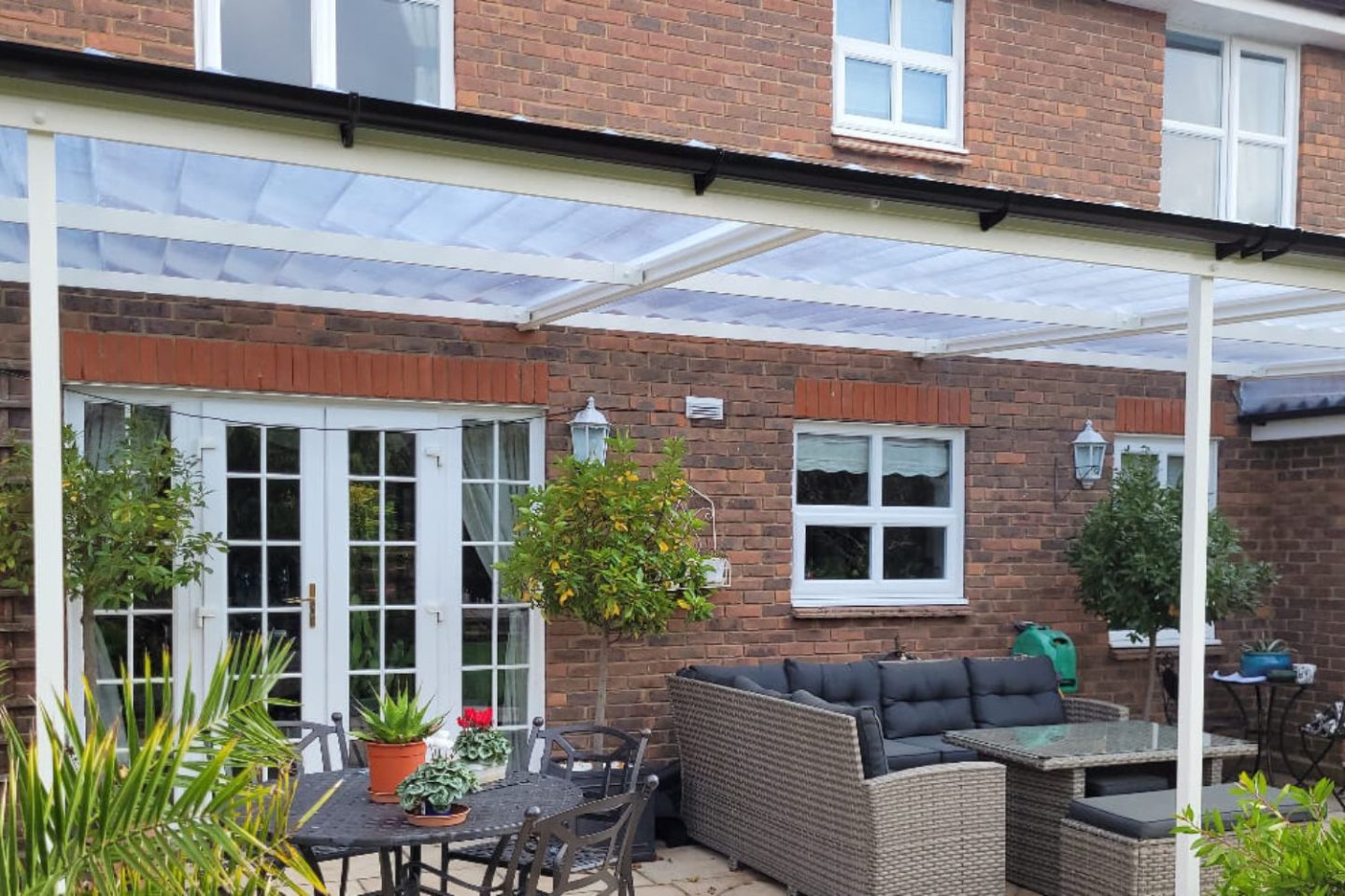 Glass veranda attached to red brick house with wicker garden chairs and lush plants