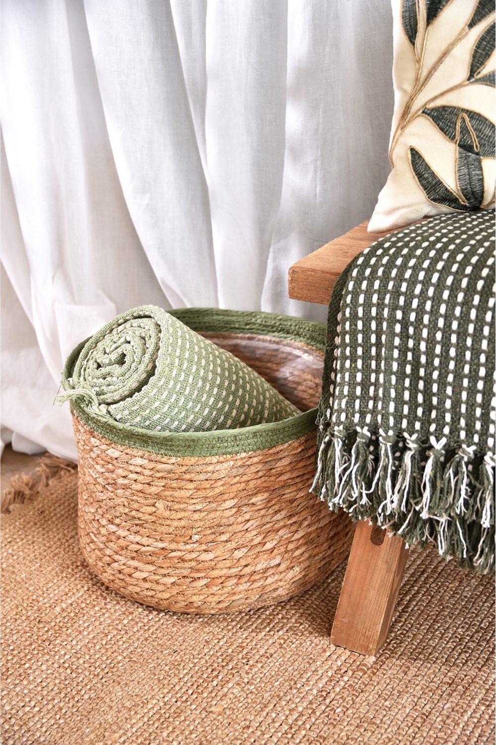 Woven basket holding green rug next to wooden chair with green throw on jute rug