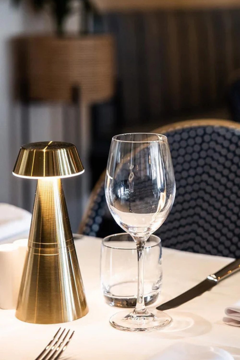 Restaurant table with wine glass and gold lamp in front of a blue chair