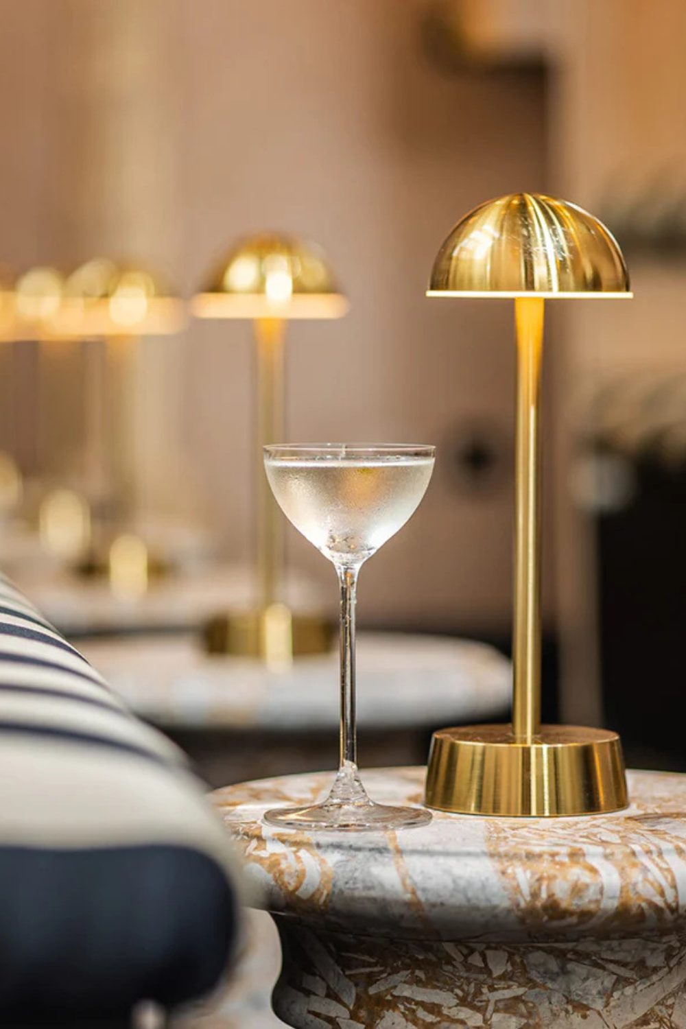 Row of gold table lamps on marble tables with wine glass in foreground