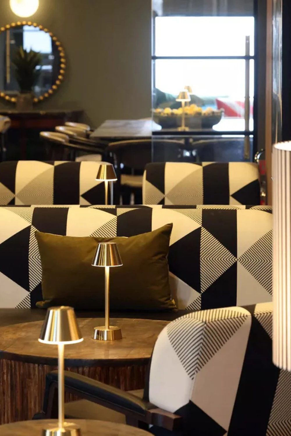 Restaurant with wooden tables, black and white geometric printsofas and gold lamps