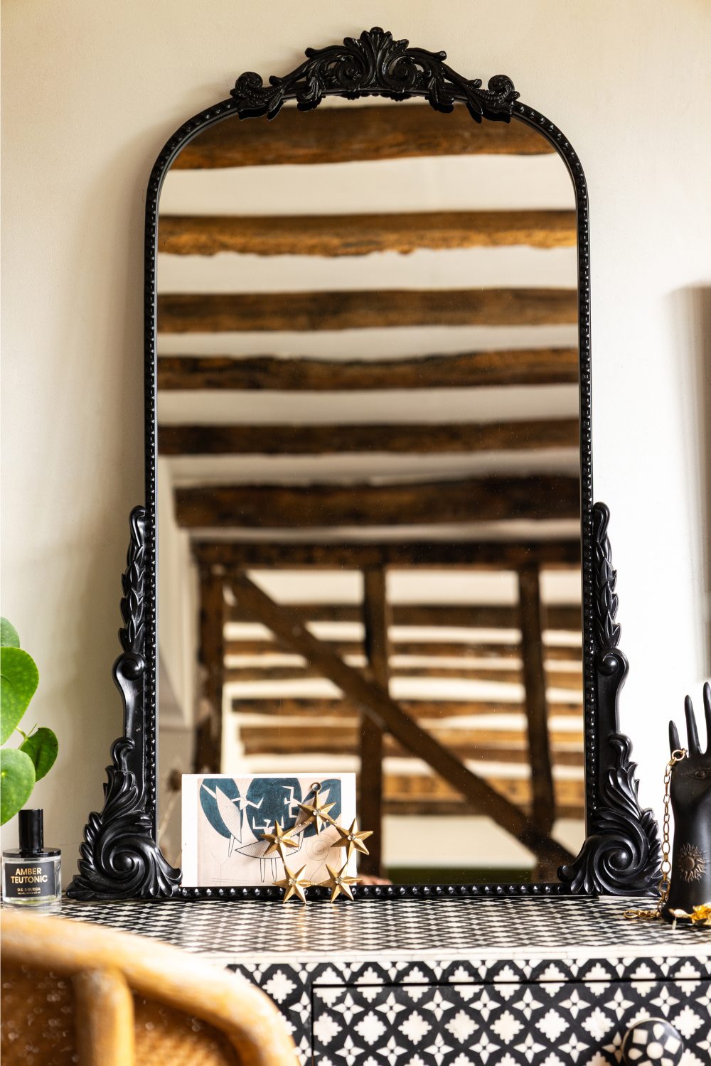 Black-framed mirror reflecting wooden beams on black and white patterned table