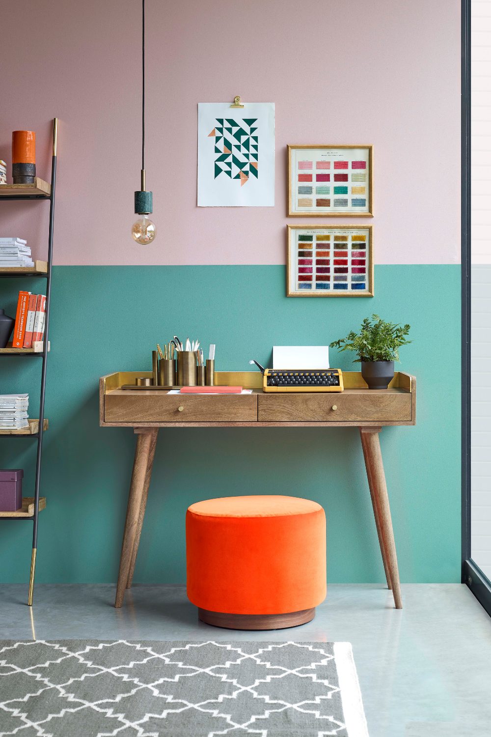 Mint green home office with white desk, black chair, framed black&white prints and black shelving unit holding globe, plants and books