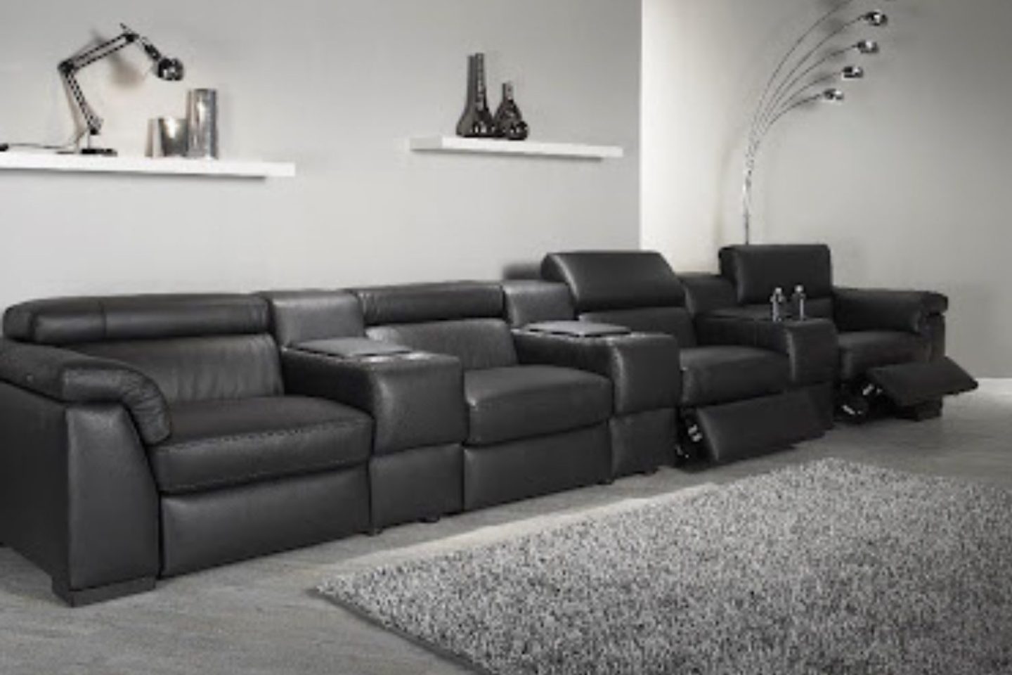Long black sofa with built-in tables in grey living room next to silver lamp
