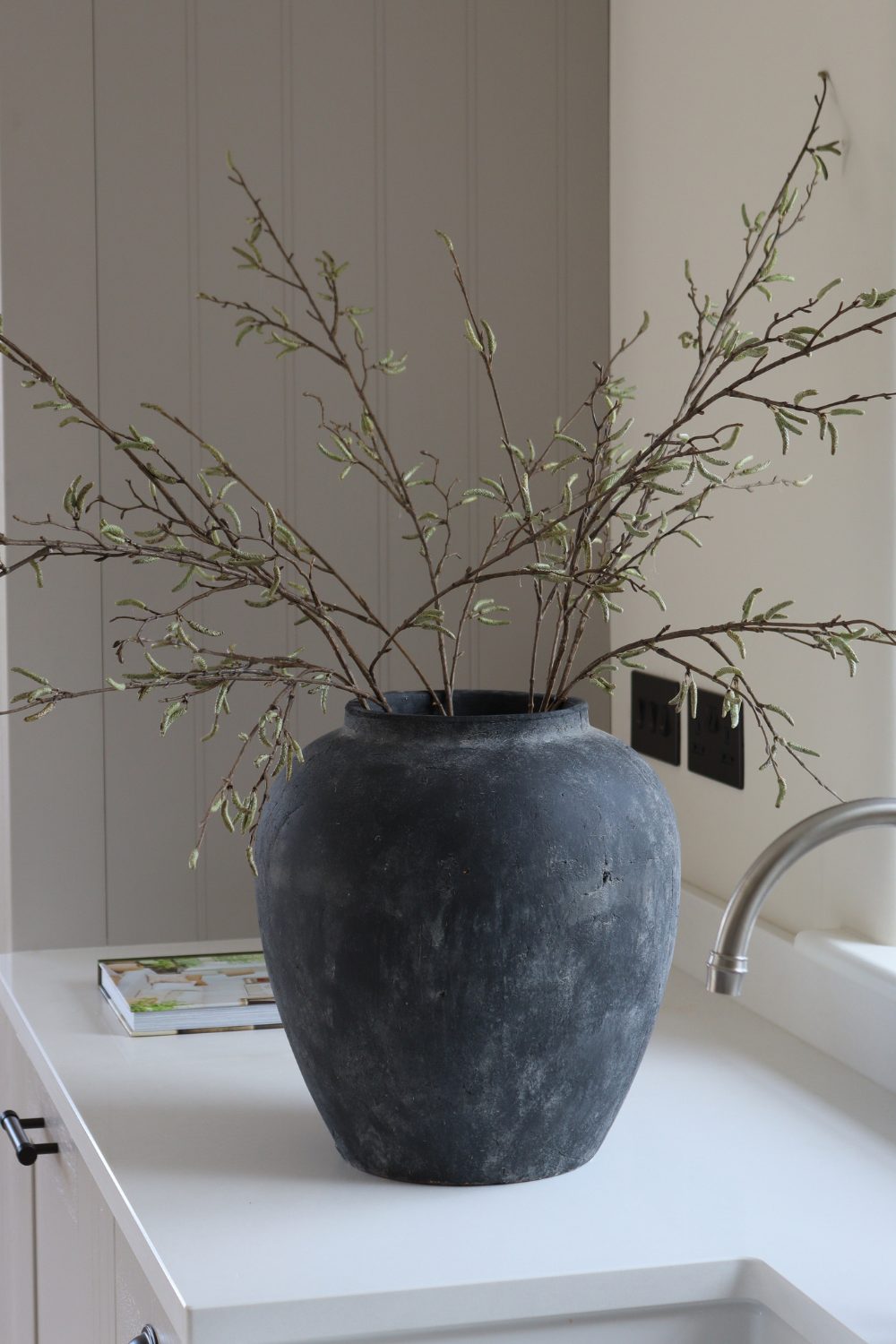 Black stoneware vase holding branches on white counter
