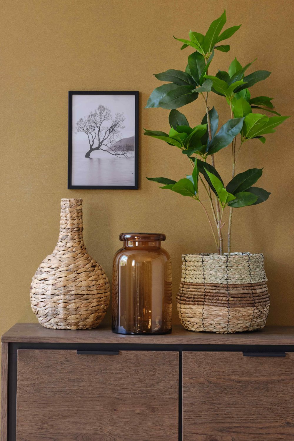 Woven vases and pot holding plant on wooden cabinet against brown wall