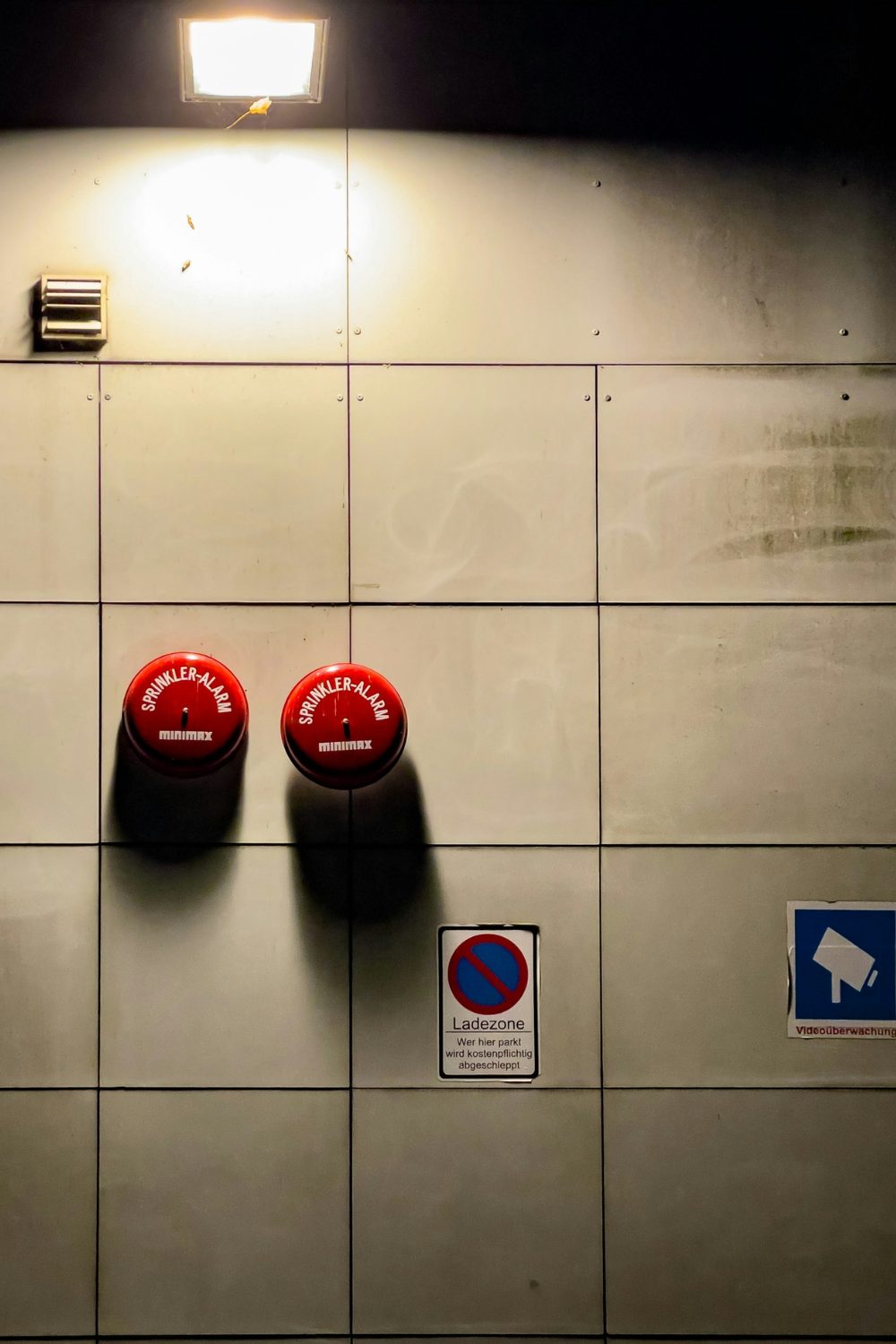 Two red fire alarms on a white panelled wall lit by a fluorescent light