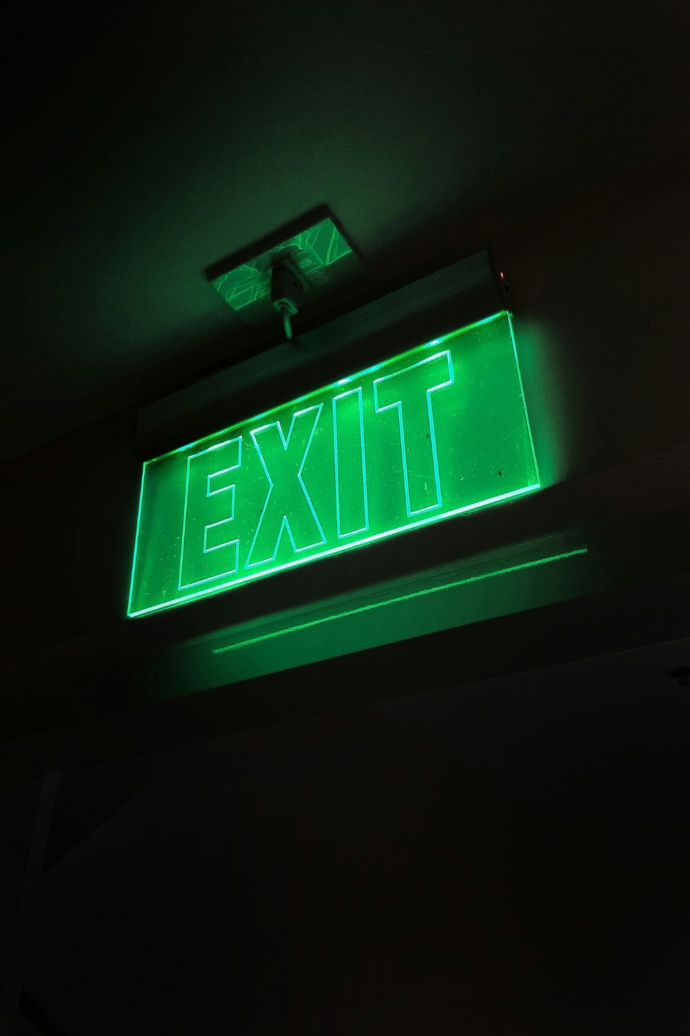 Green Exit sign lit up surrounded by darkness
