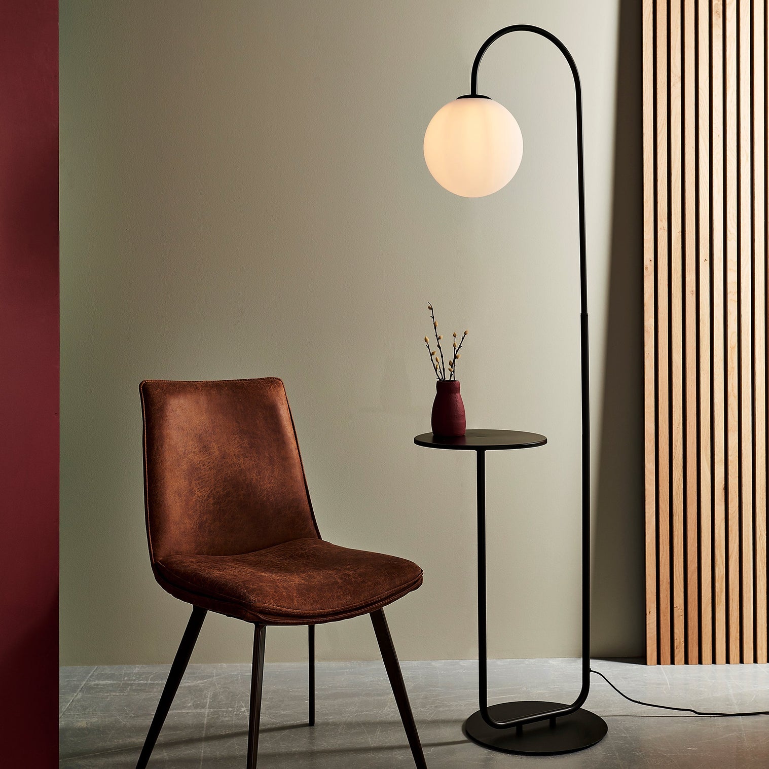 Black standing lamp next to brown chair in grey room with wooden feature wall