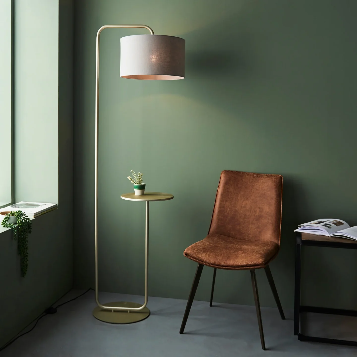 Gold standing lamp in green room next to brown chair and wooden table