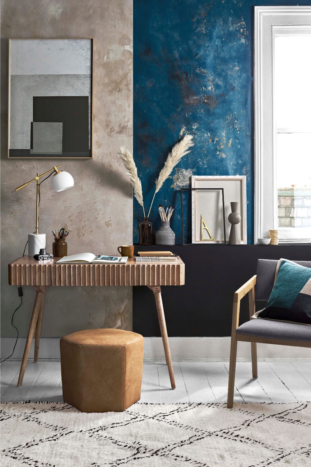 Blue and grey home office with orange pouffe, grey chair, and desk with corrugated edge on white wood floor