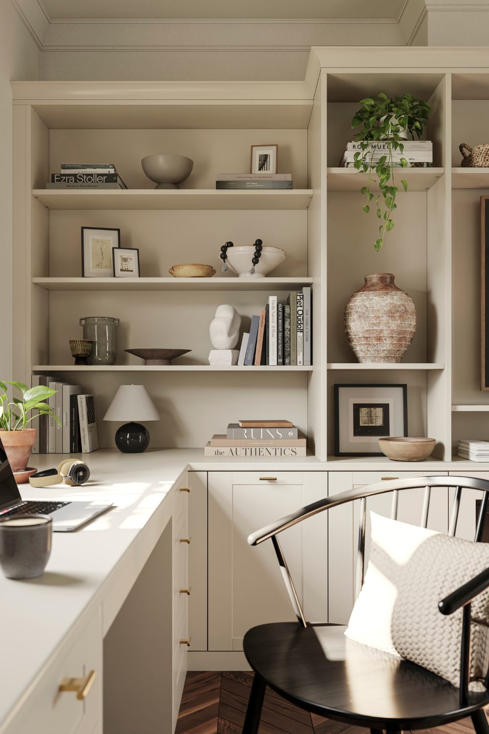 White home olffice with tall built-in shelves holding books and plant pots, black chair with white cushion and laptop on desk