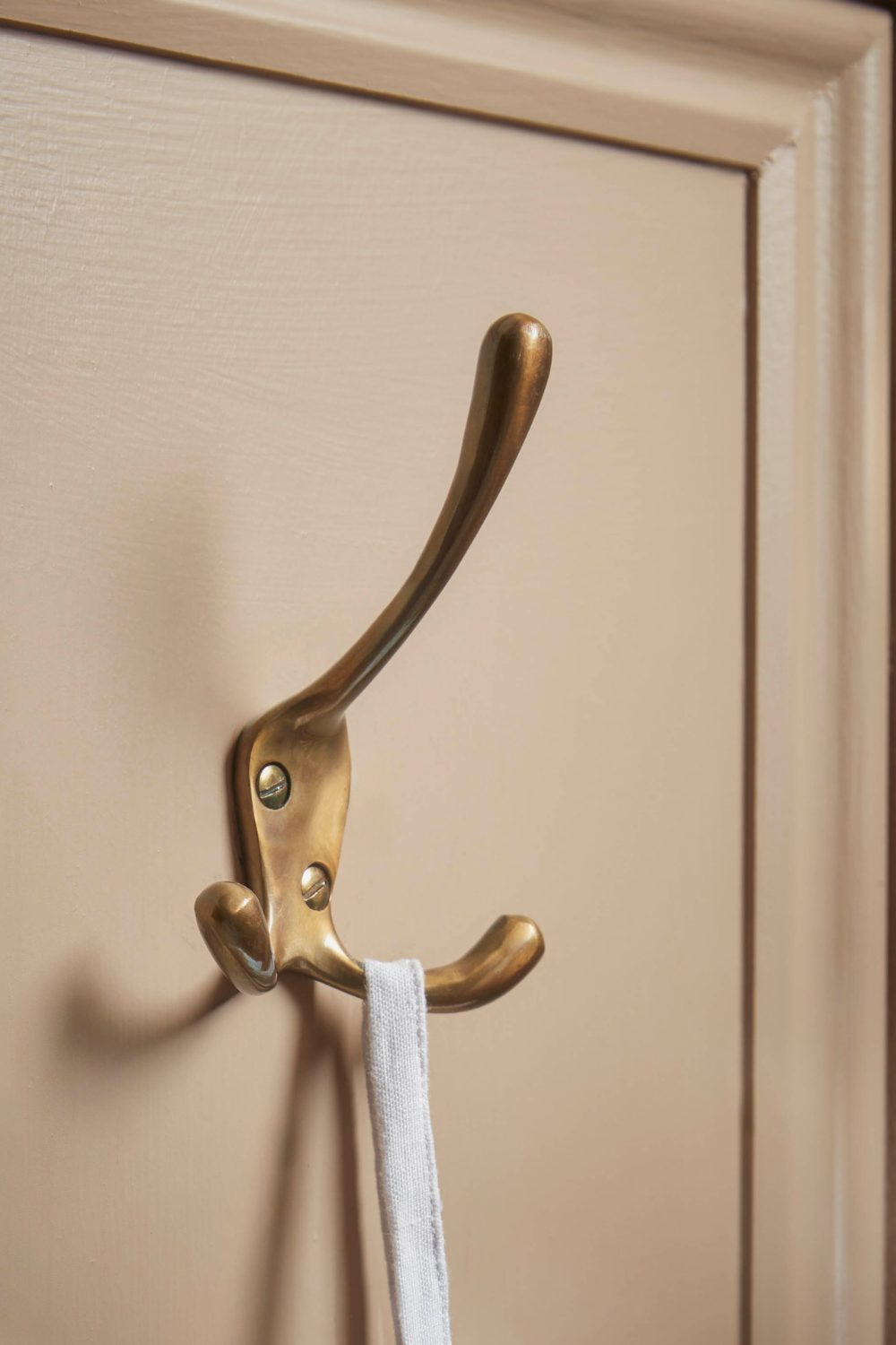 Brass coathook on white door holding a white strap