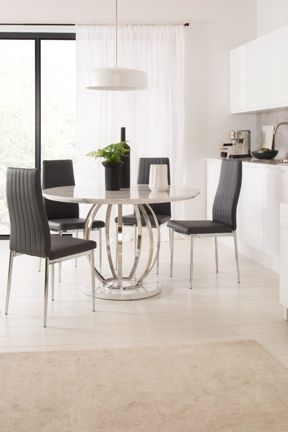 White kitchen with grey chairs, white lampshade and white table with curved metal stand in front of window with garden view