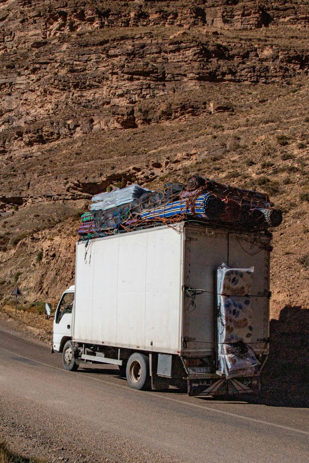 White truck with rugs roped to the top and back driving through rocky desert landscape