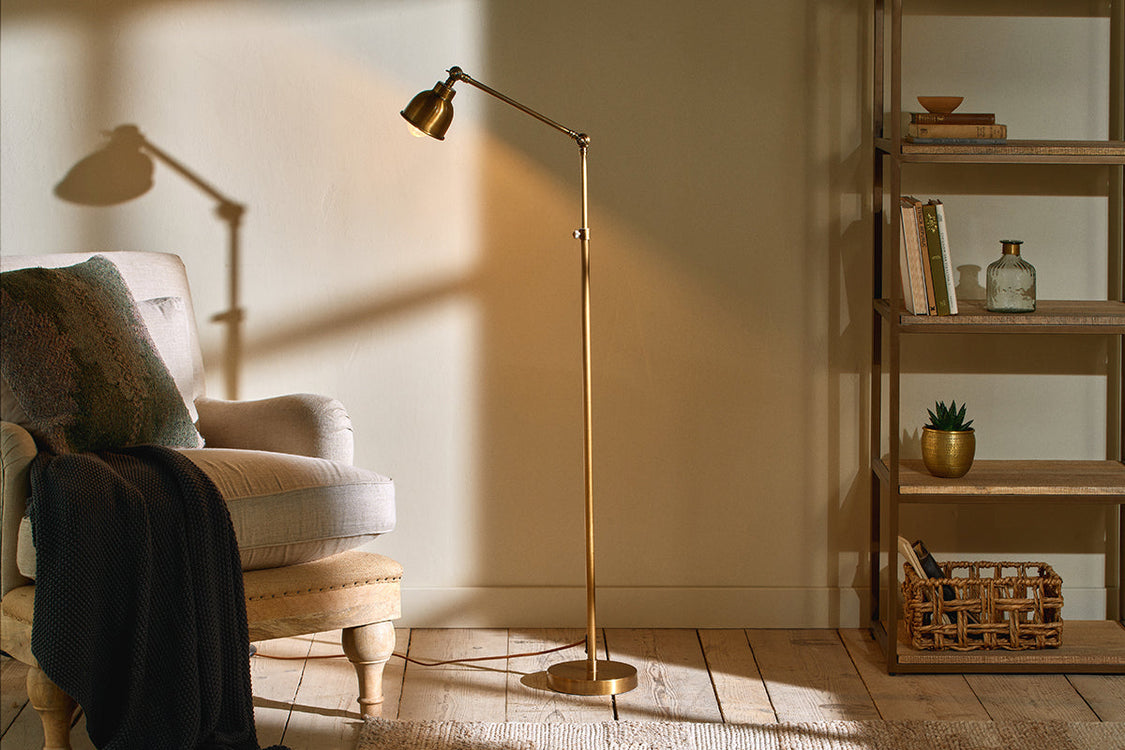 Gold standing lamp next to white armchair and shelving unit in white room with wooden floor