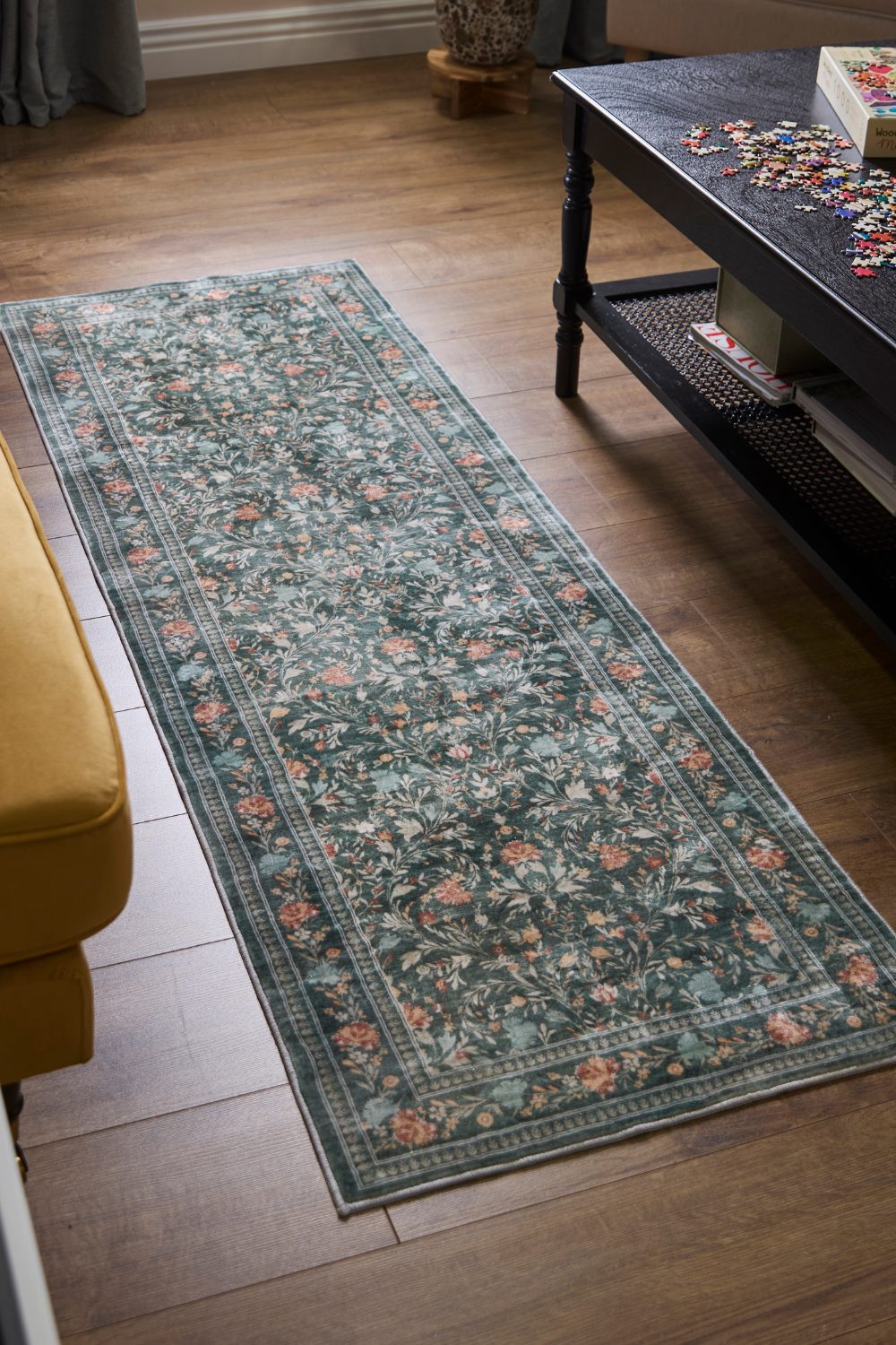 Vinatge-style rug on wooden floor next to mustard yellow sofa and black coffee table holding puzzle pieces
