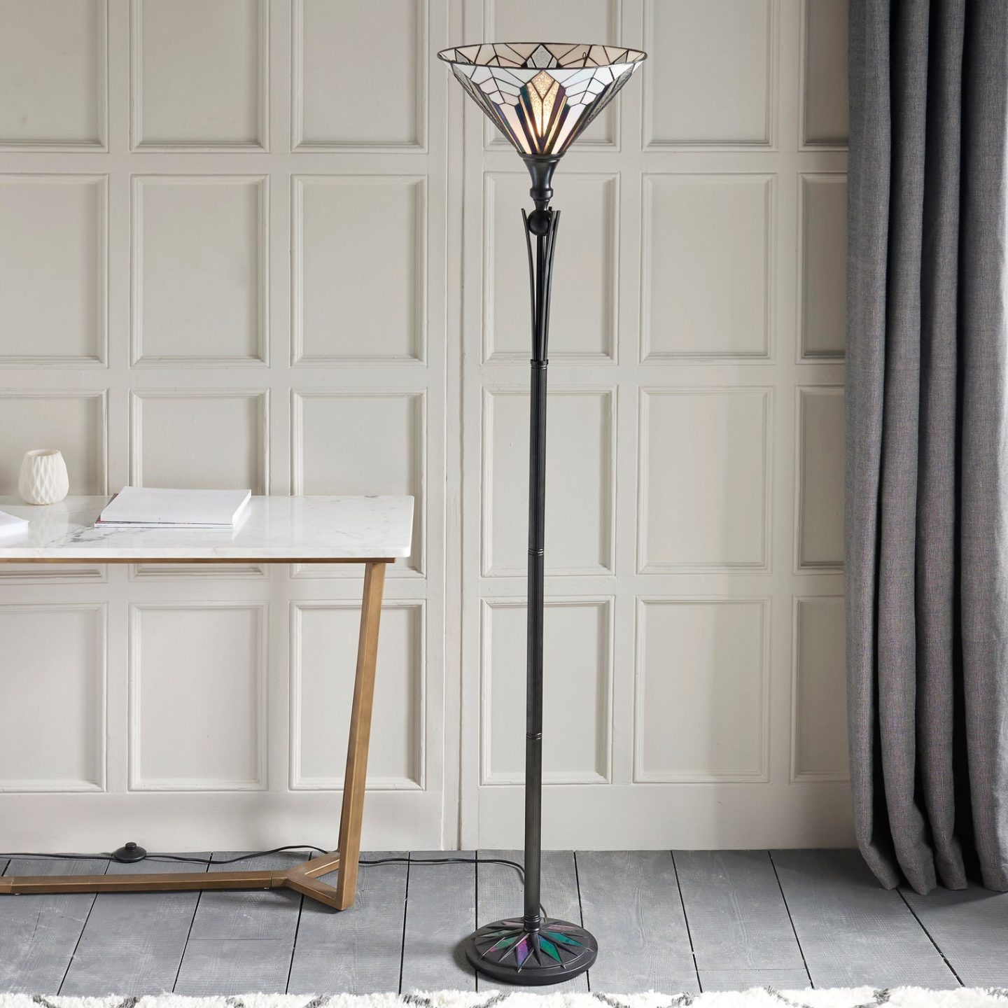Standing lamp with Tiffany glass shade and white table in white panelled room with grey wooden floor