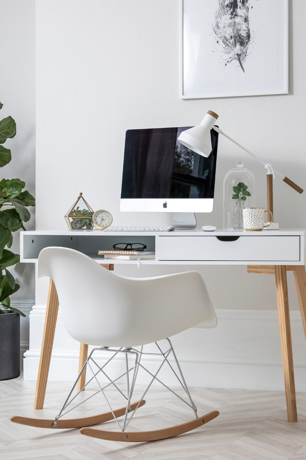 White chair and desk holding computer, white lamp and white mug under white framed print