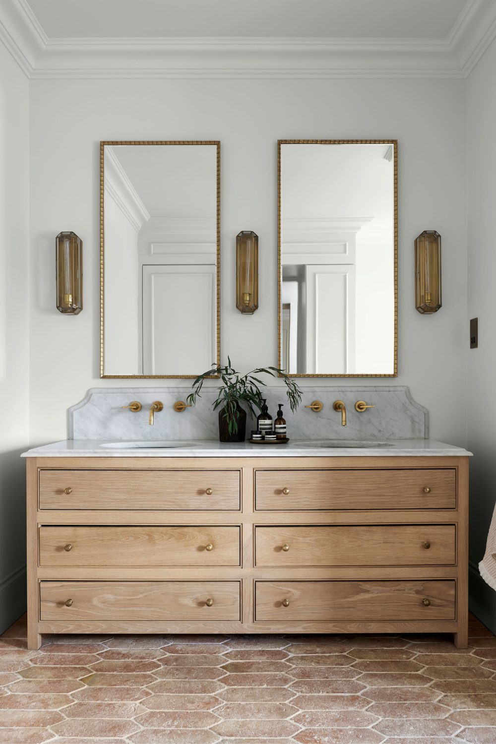 Bathroom with double sinks on top of wooden cabinet with gold-framed mirrors