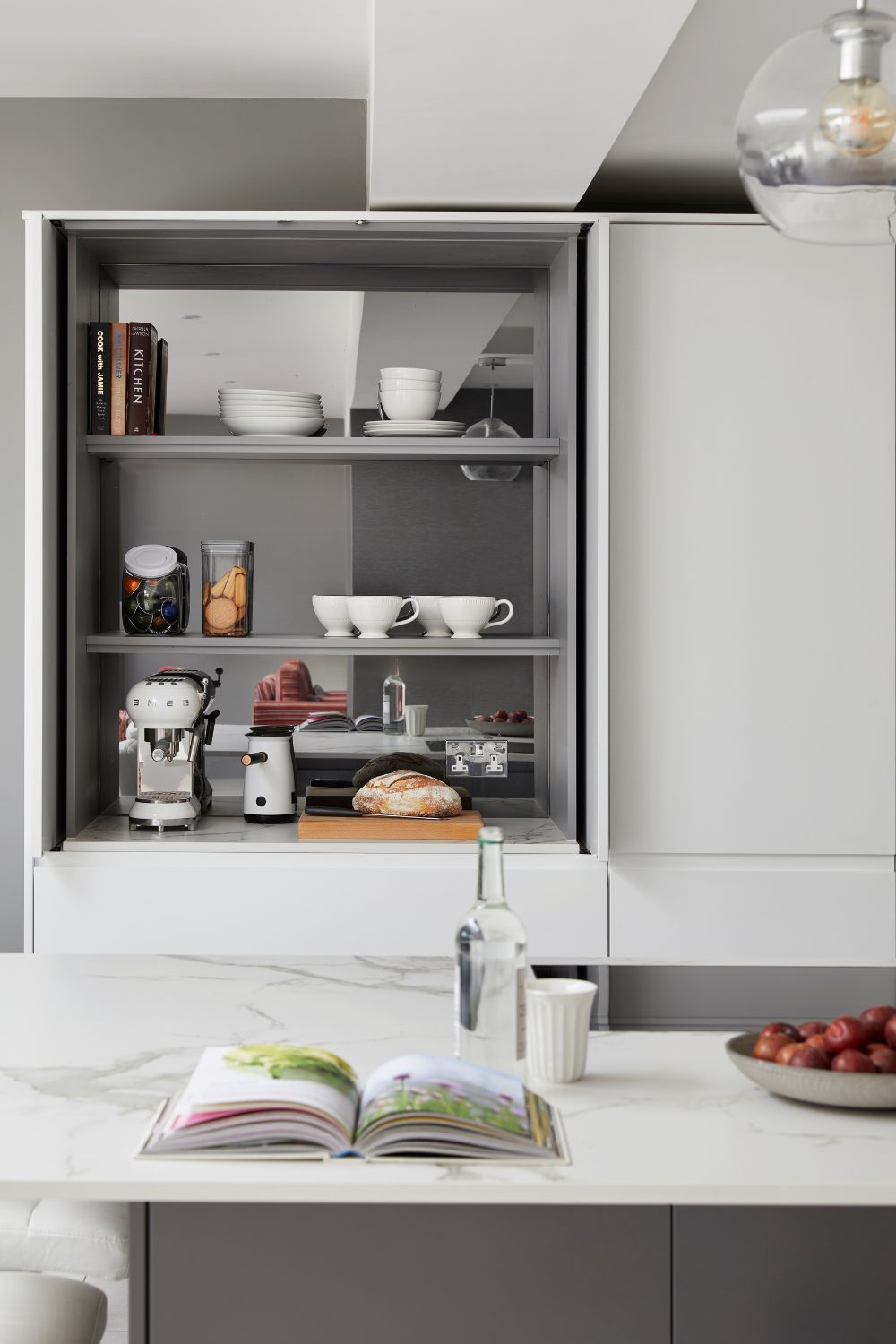 Grey kitchen with open shelving holding cookbooks, jars, white cups and breadboard