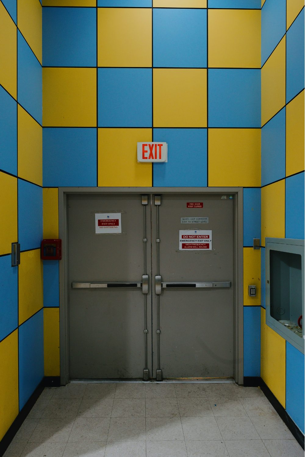 Grey double doors and red Exit sign in blue and yellow tiled wall
