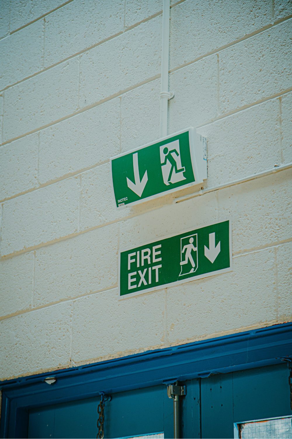 Green Fire Exit signs in white wall above blue door