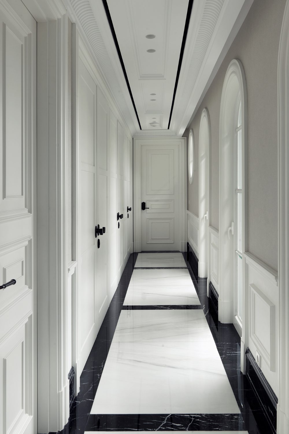 White hallway lined with white doors with a black and white marble floor