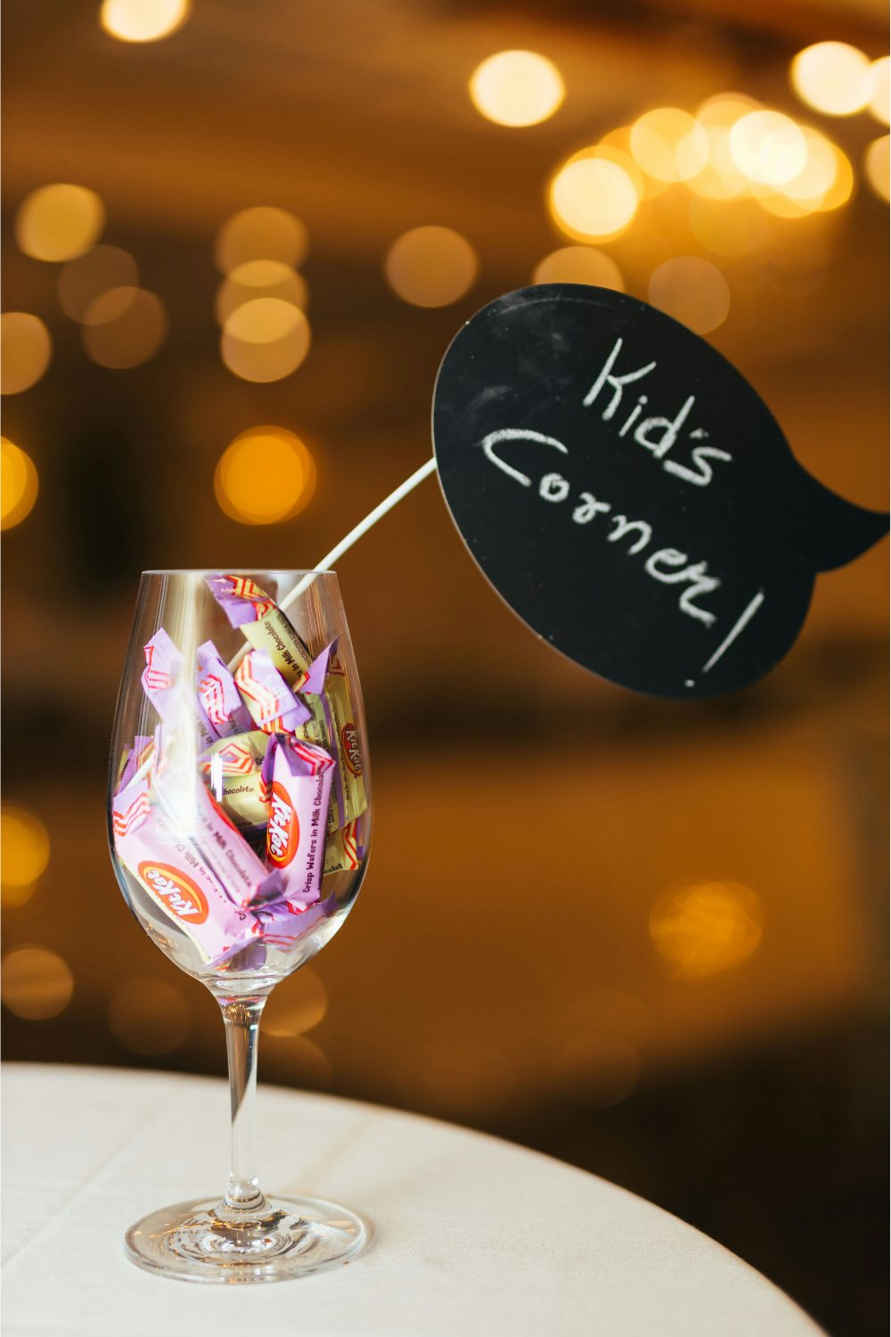 Wine glass filled with sweets and Kid's Corner sign on white table