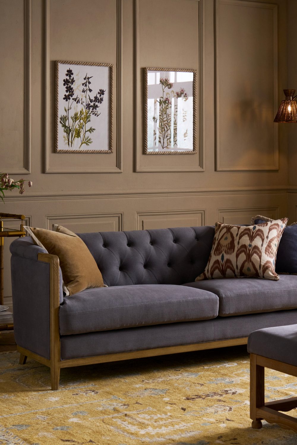 Navy sofa on mustard yellow rug in wood-panelled living room with framed botanical prints