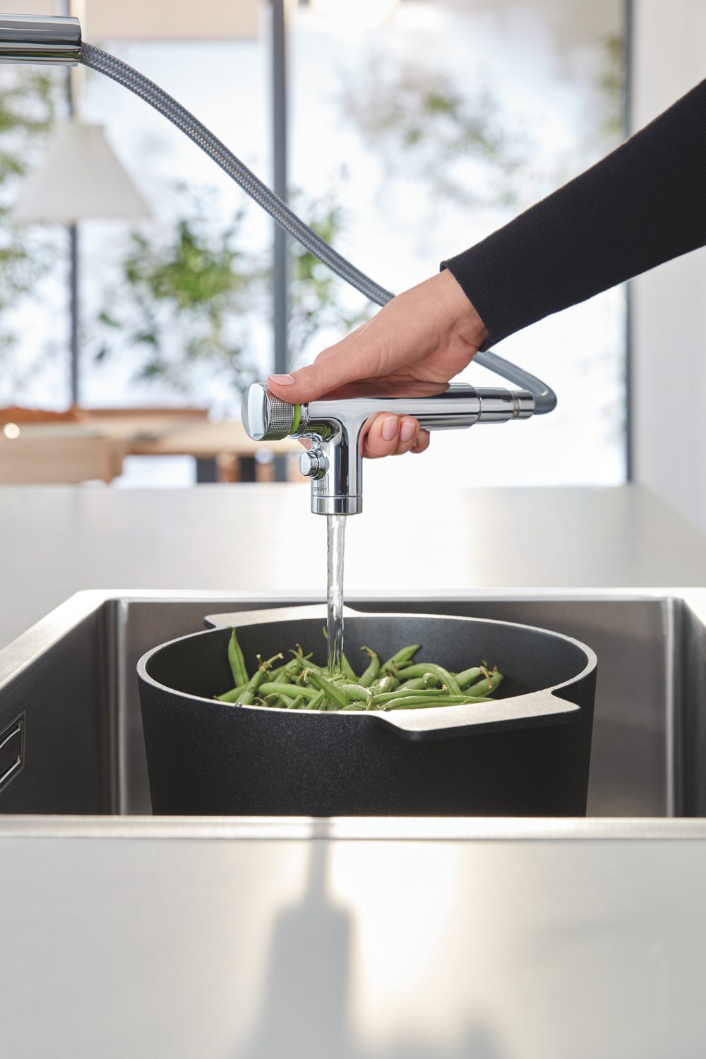 Extension tap pouring water over pan of green beans in deep sink