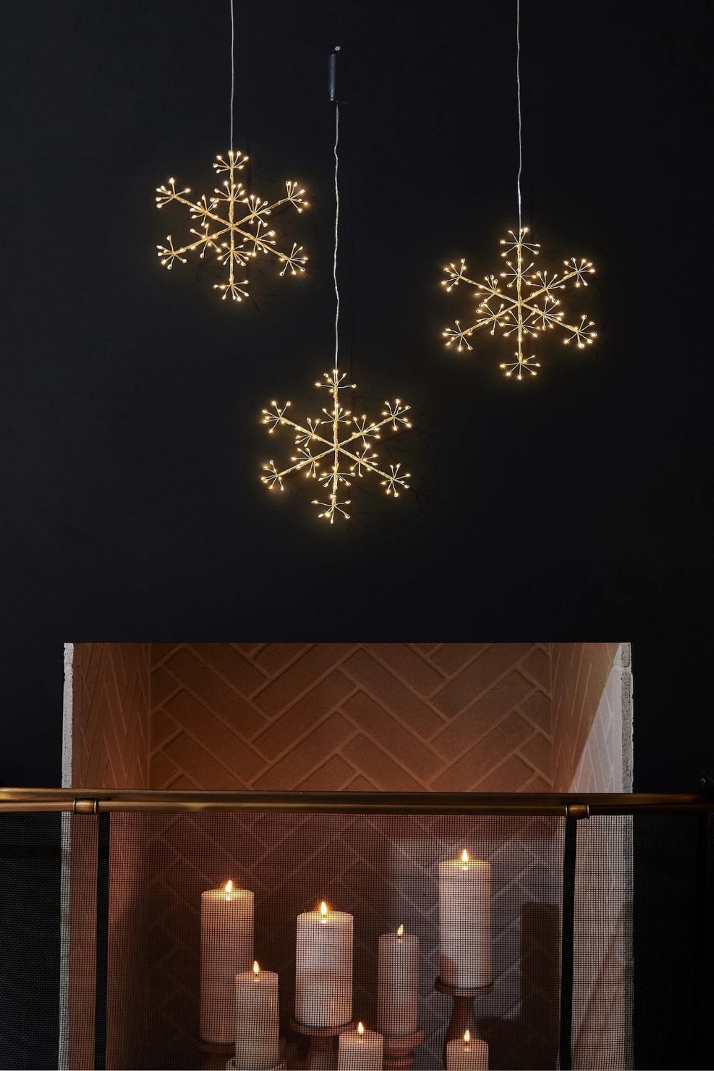 Three snowflake lights hanging above lit white candles in brick fireplace
