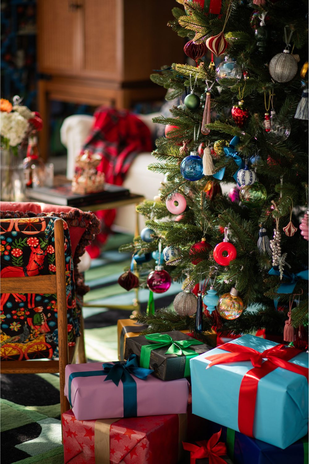 Christmas tree with colourful decorations and wrapped presents at the bottom, with white sofa in background