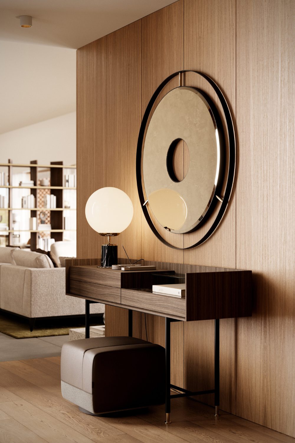 Wooden desk and brown pouffe under round mirror on wooden wall, with brown sofa and shelving in background