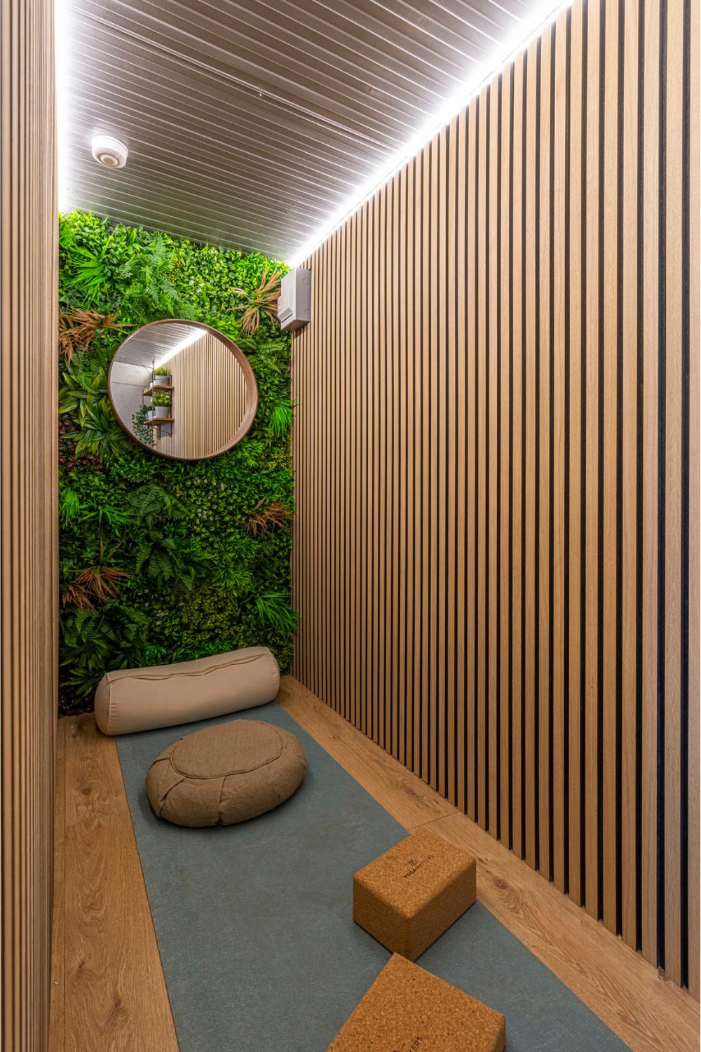 Small wood-panelled room with a plant wall, neon ceiling lighting, and yoga equipment on wood floor