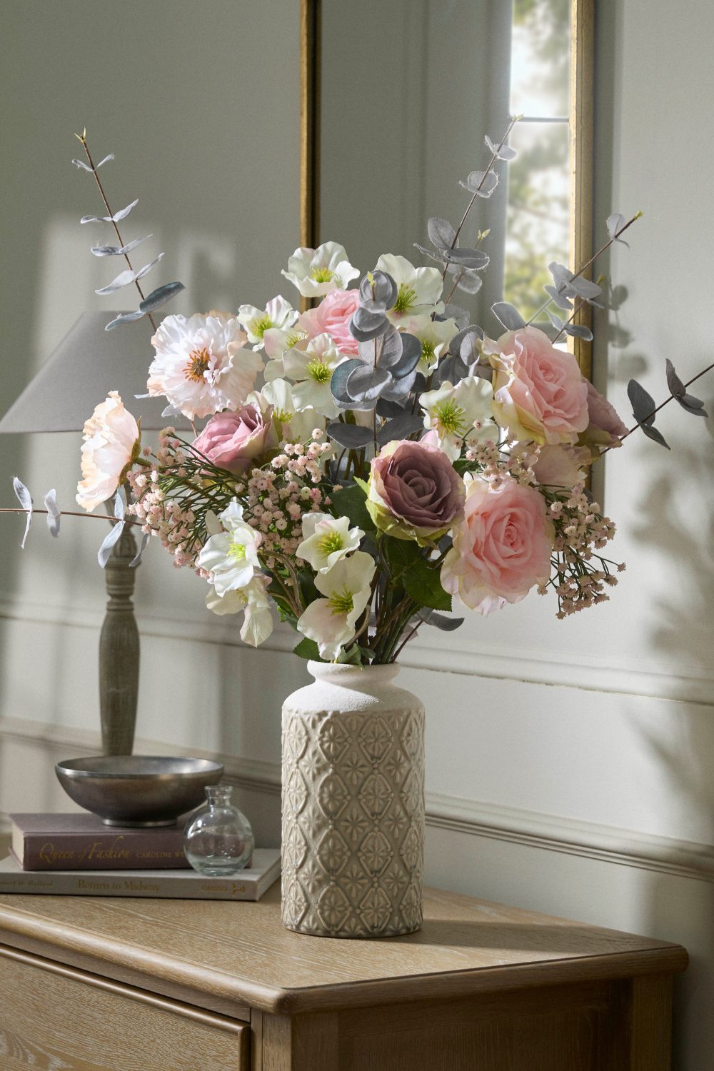 White patterned vase on wooden table holding bouquet of pink, white and purple flowers