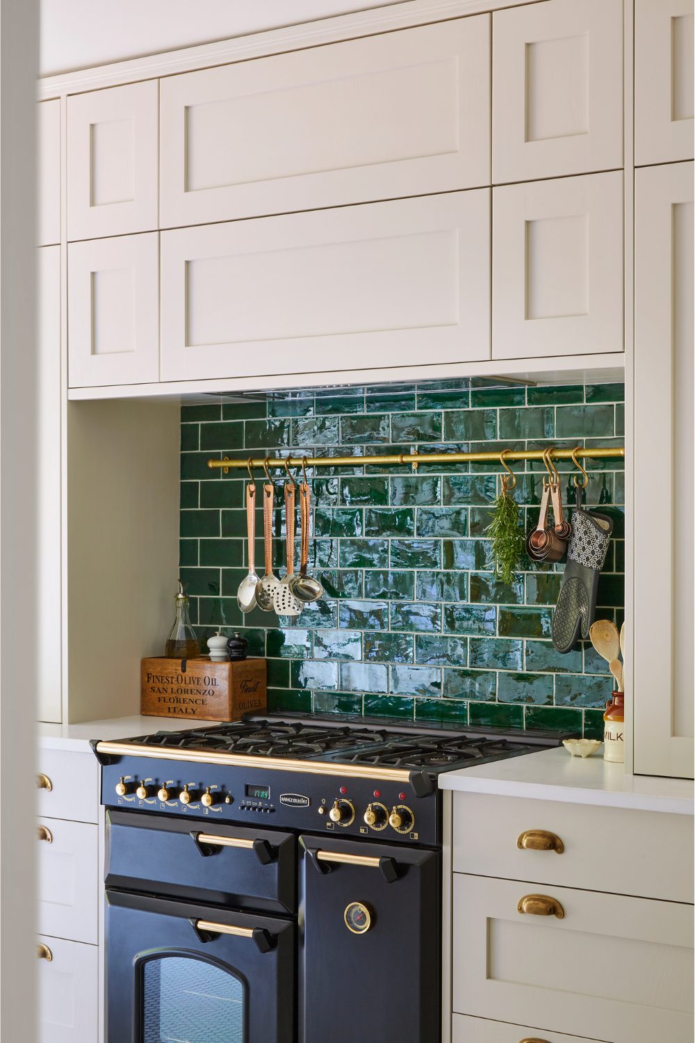 White kitchen with teal tiled backsplash, navy oven and hanging utensils