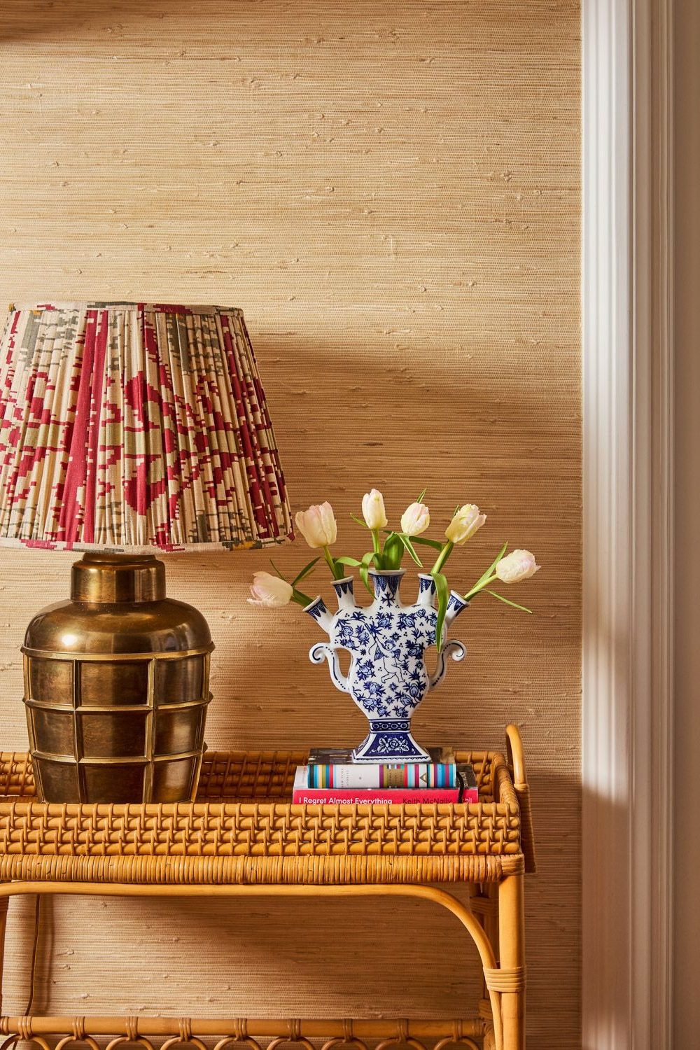 Wicker table holding gold lamp with red and white shade, and blue & white vase holding white tulips