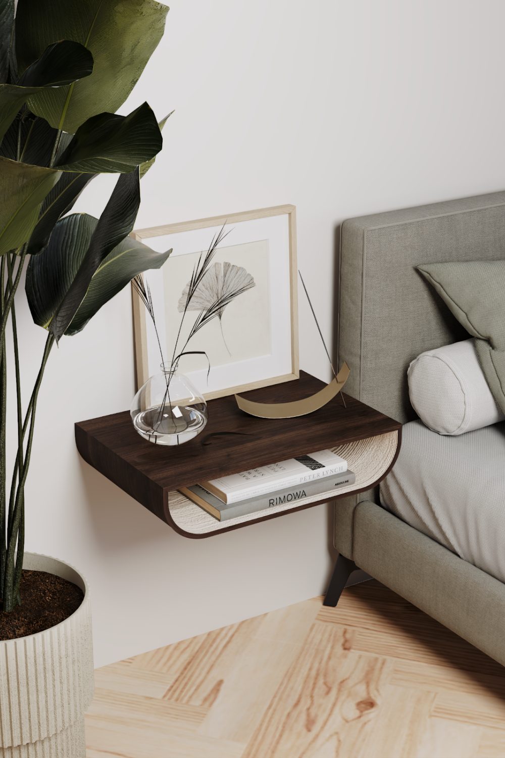 Grey bed and potted tree next to floating wooden nightstand holding framed print and books