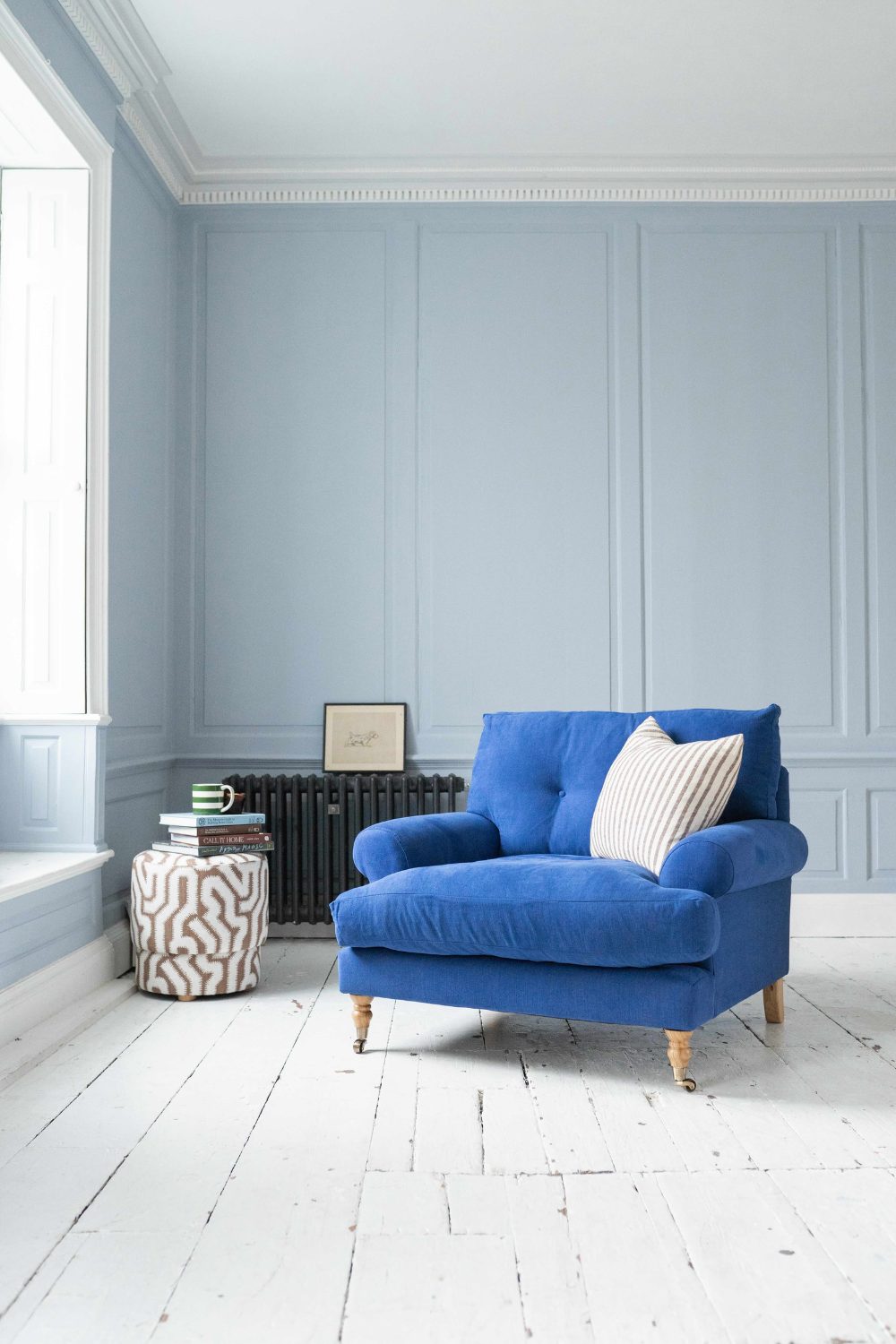 Bright blue armchair in muted blue living room with white wooden floor